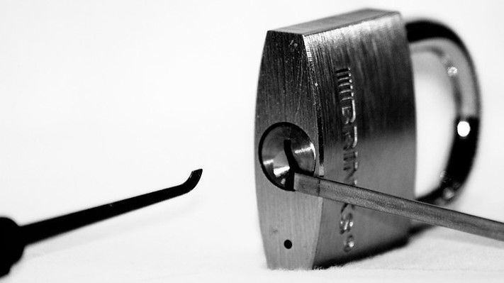 A lock with a tension bar inside, with a a lock pick about to be inserted.