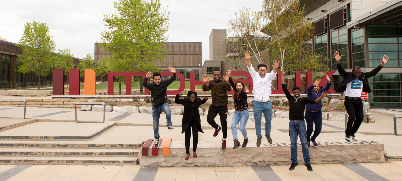 Group of international students jumping in front of the Mohawk College sign