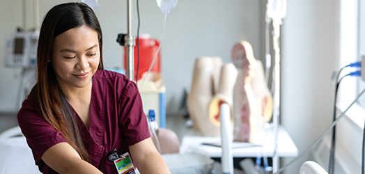 Mohawk College nursing student working with medical equipment, mannequins in the background.