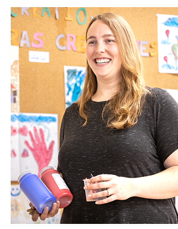 Camille smiling holding paint bottles.