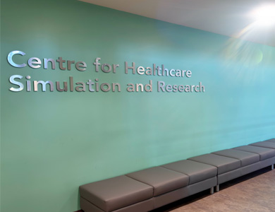 View of wall signage-lettering on light blue-green coloured background at front entrance of the Centre with text written as 'Centre for Healthcare Simulation and Research'.