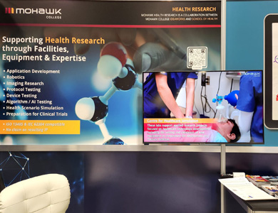 Partial view of Mohawk College booth at MedTech Conference with banner listing items from collaboration between Ideaworks and the School of Health