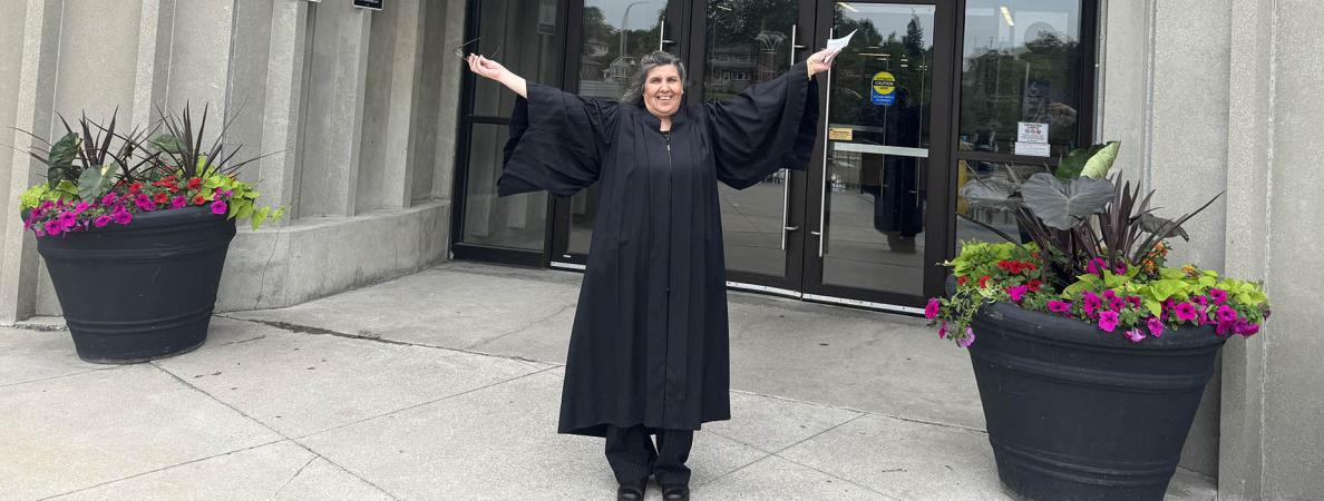 Rosalind Phillips wearing a graduation gown standing infront of an entrance to Mohawk College Fennell campus.