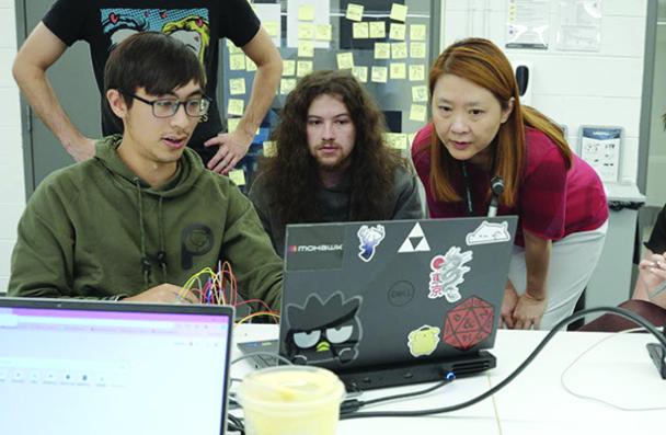 A group of Game Design students and a professor gathered around a laptop.