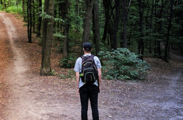 A man standing in a forest with two very different paths in front of him.