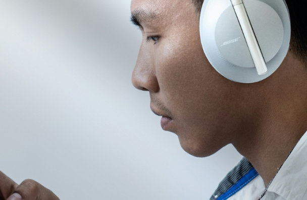 An image of an Asian man in profile.  He is wearing headphones and looking at his phone.