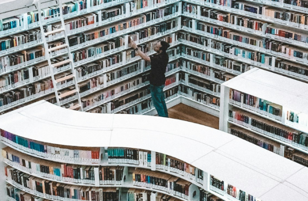 An image of a large library with a man looking at a book.