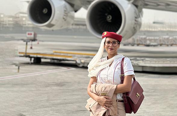 Smiling woman in airline attendant uniform with headscarf in front of commercial jet