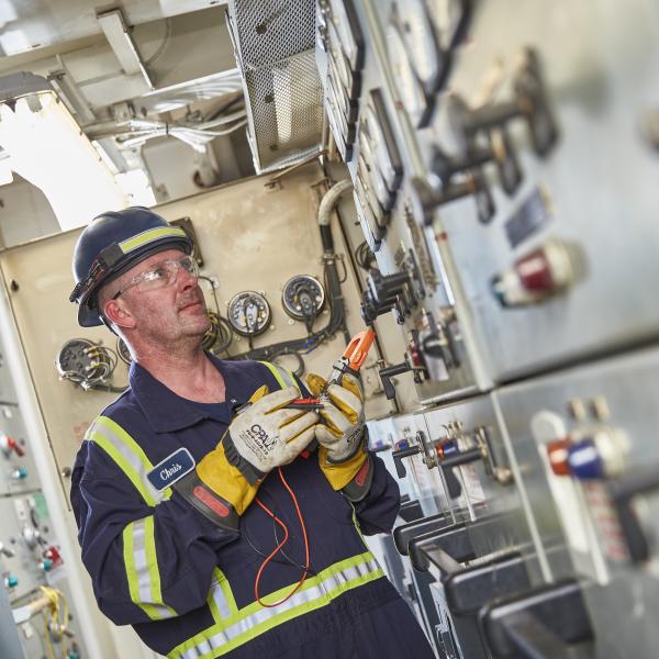 Man checks electrical levels on ship deck.